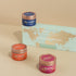 Three DiyaAromes candles with colorful lids on a beige surface, with a world map in the background.